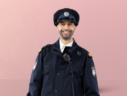 Agent Ibrahim in uniform met politiepet en microfoon, tegen een roze achtergrond.
