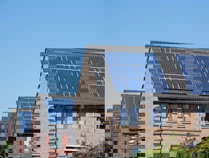 Drie huizen met zonnepanelen op de daken, onder een heldere blauwe lucht.