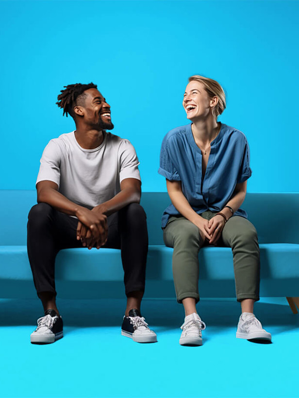 Twee mensen zitten op een lichtblauwe bank tegen een felblauwe achtergrond, met een groene plant rechts op de vloer.
