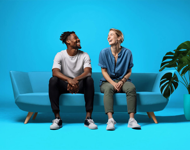 Twee mensen zitten op een lichtblauwe bank tegen een felblauwe achtergrond, met een groene plant rechts op de vloer.