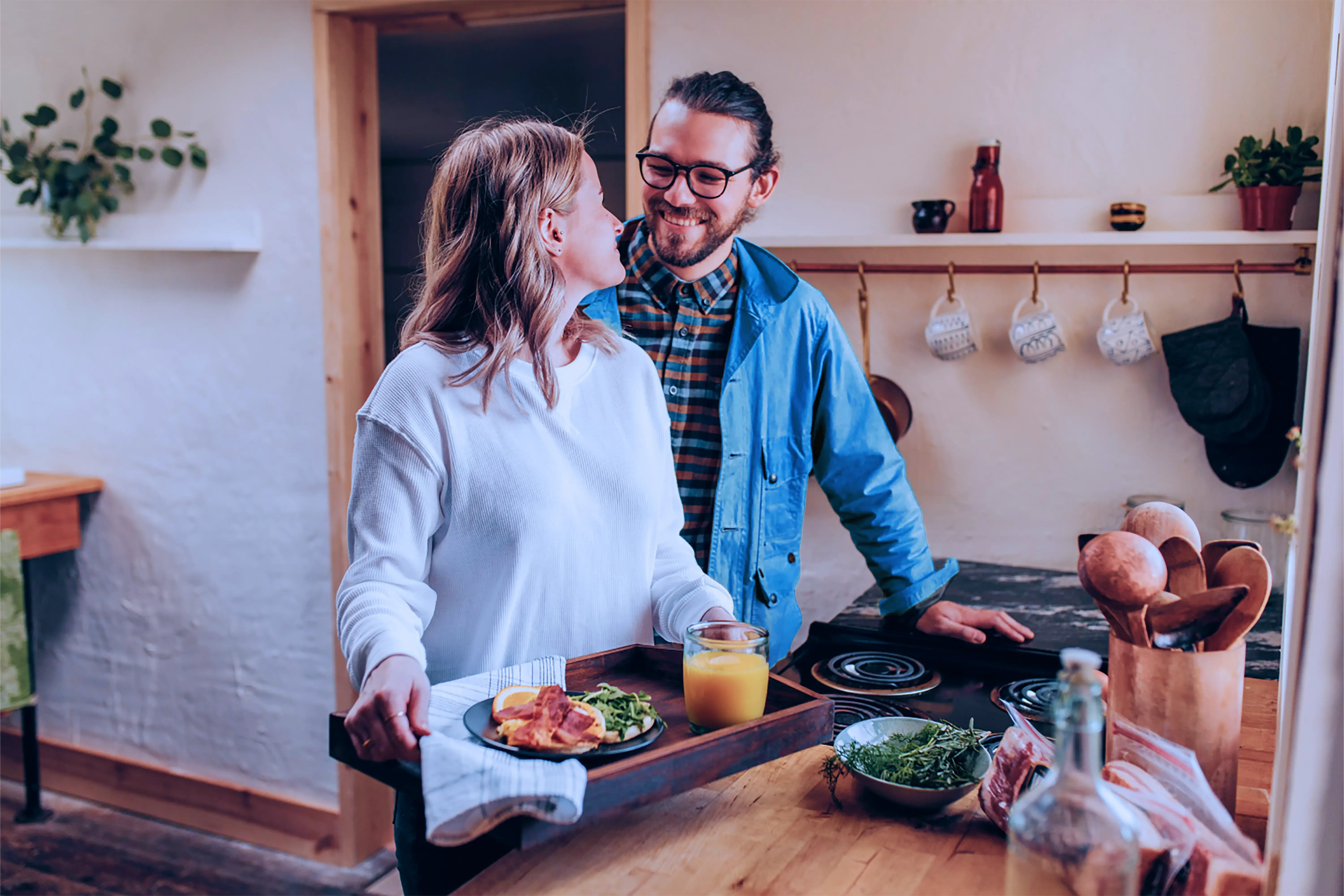 Vrouw in een keuken met een dienblad vol ontbijt, kijkend naar iemand achter haar.