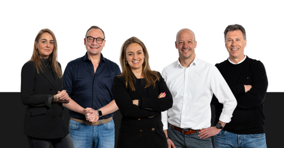 Vijf mensen in professionele kleding poseren samen voor een zwarte achtergrond, met oprechte gezichten en zelfverzekerde houdingen.