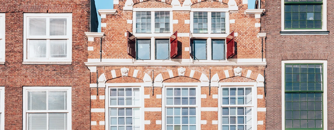 Roodstenen gebouw met witte accenten en een gedetailleerde gevel, omringd door twee moderne gebouwen.