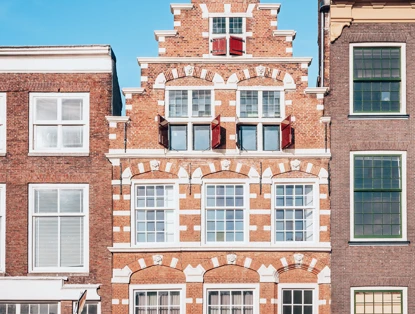 Roodstenen gebouw met witte accenten en een gedetailleerde gevel, omringd door twee moderne gebouwen.
