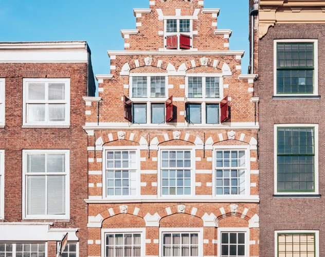 Roodstenen gebouw met witte accenten en een gedetailleerde gevel, omringd door twee moderne gebouwen.