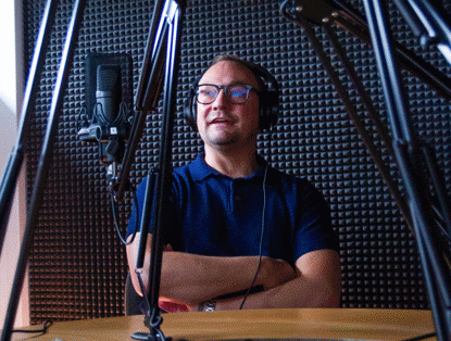 Een persoon met een hoofdtelefoon zit in een geluidsstudio, omringd door microfoons en geluidsisolatiepanelen.