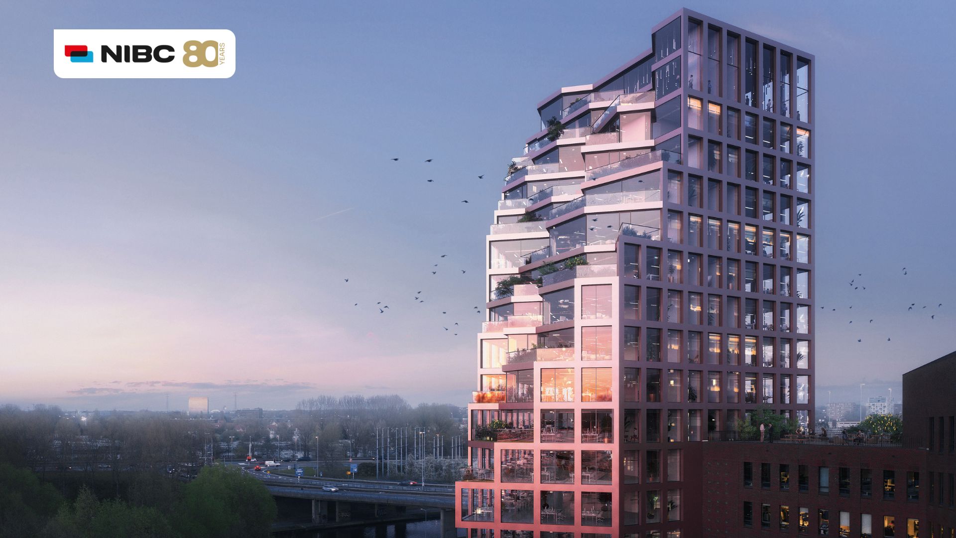 Moderne hoge woontoren met glazen balkons en een zachte roze tint, gelegen naast een snelweg onder een heldere lucht.