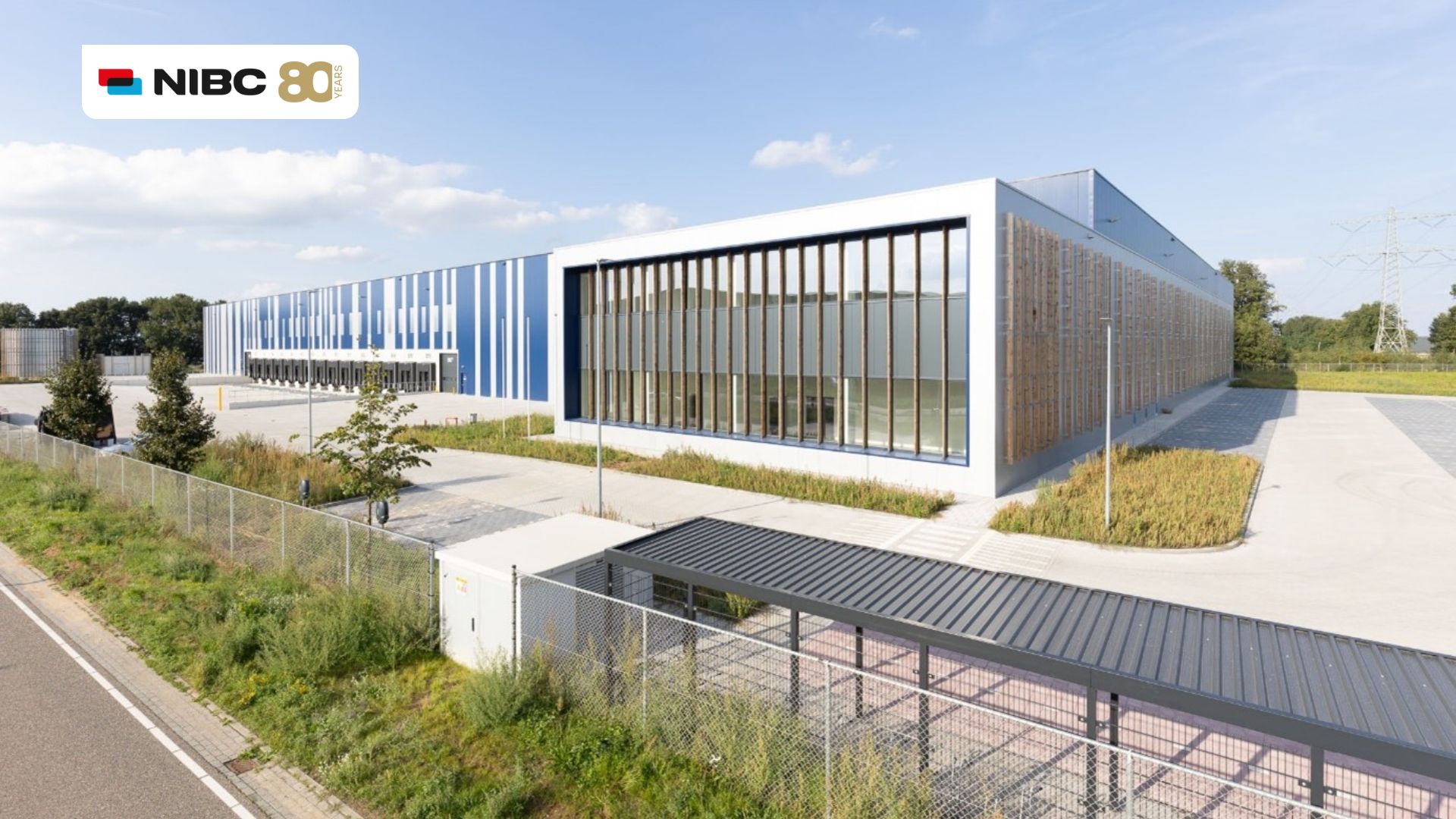 Moderne kantoorgebouwen met grote ramen en blauwe panelen, gelegen langs een straat en omringd door groen.