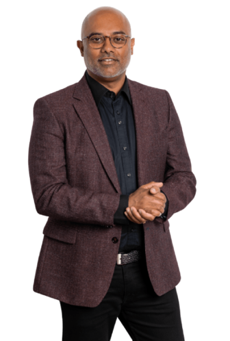 Amer Jagesar in een stijlvol gemêleerd jasje, met een zwart overhemd en een donkere broek, die zijn handen in een gebarenhouding houdt.