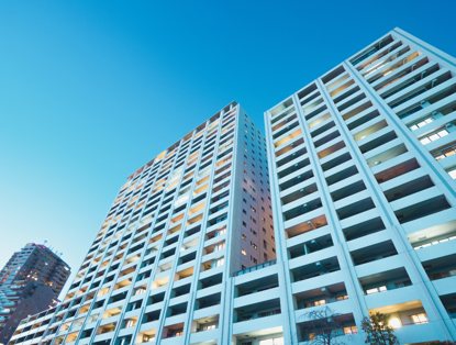 Modern apartment complexes under a clear blue sky, with lights in the windows for a lively appearance.