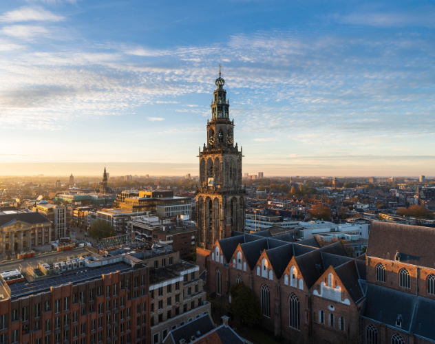 Uitzicht op de toren van de Grote Kerk in Zwolle, omringd door de stad en een kleurrijke lucht tijdens de zonsondergang.