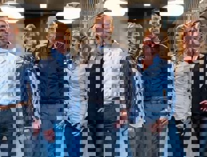 Vijf collega's in zakelijke kleding staan ontspannen in een kantooromgeving.