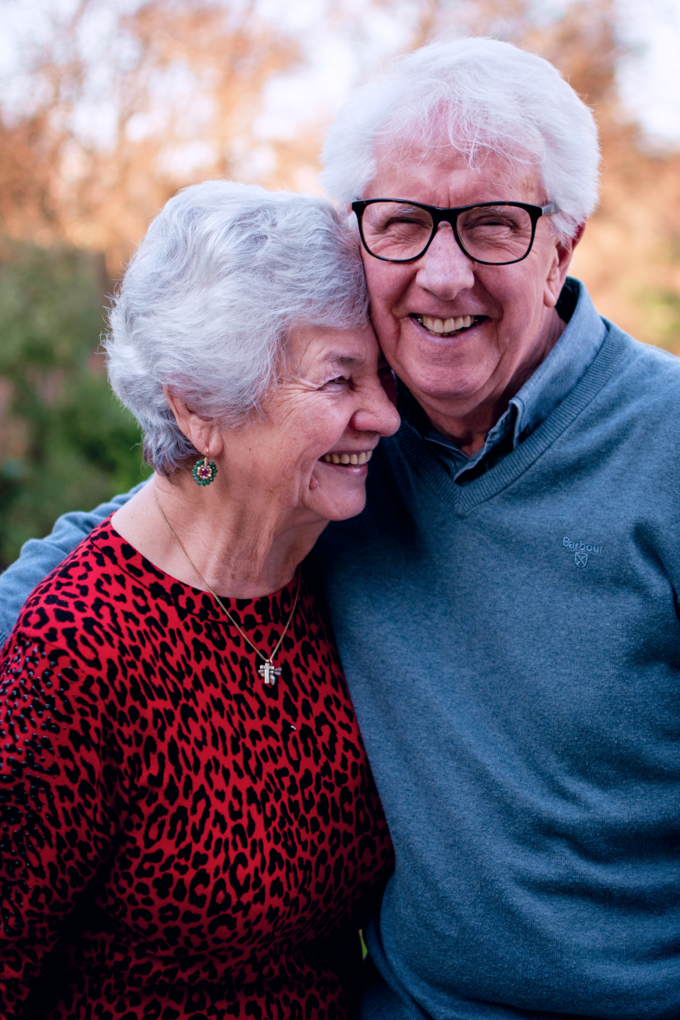 Een oudere vrouw met grijs haar en een man met grijs haar staan dicht bij elkaar en genieten van een zonnige dag in de natuur.