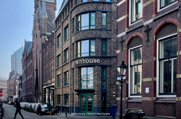 Modern townhouse met grote ramen en een groene deur, gelegen aan een straat met historische gebouwen en straatverlichting.