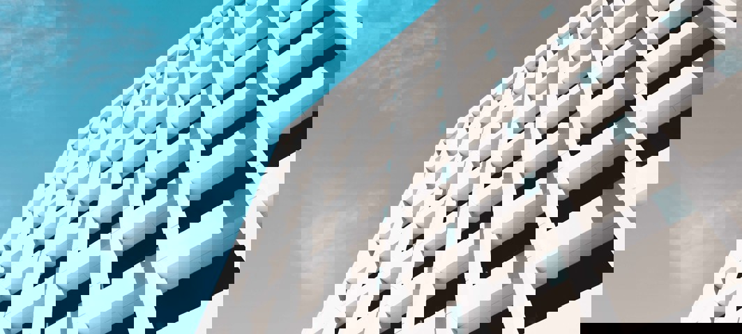 Moderne witte gevel van een gebouw met opvallende rechthoekige vensters onder een heldere blauwe lucht.