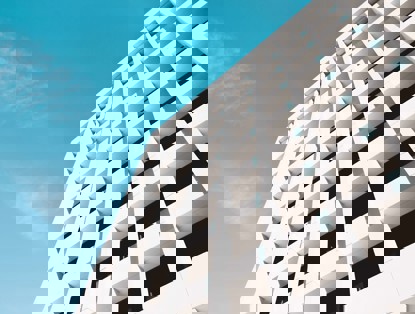 Moderne witte gevel van een gebouw met opvallende rechthoekige vensters onder een heldere blauwe lucht.