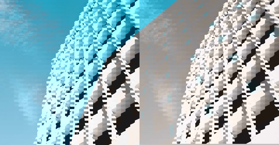 Moderne witte gevel van een gebouw met opvallende rechthoekige vensters onder een heldere blauwe lucht.