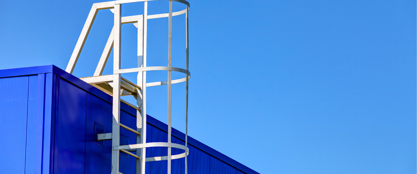 Witte ladder tegen een blauwe muur onder een heldere blauwe lucht.