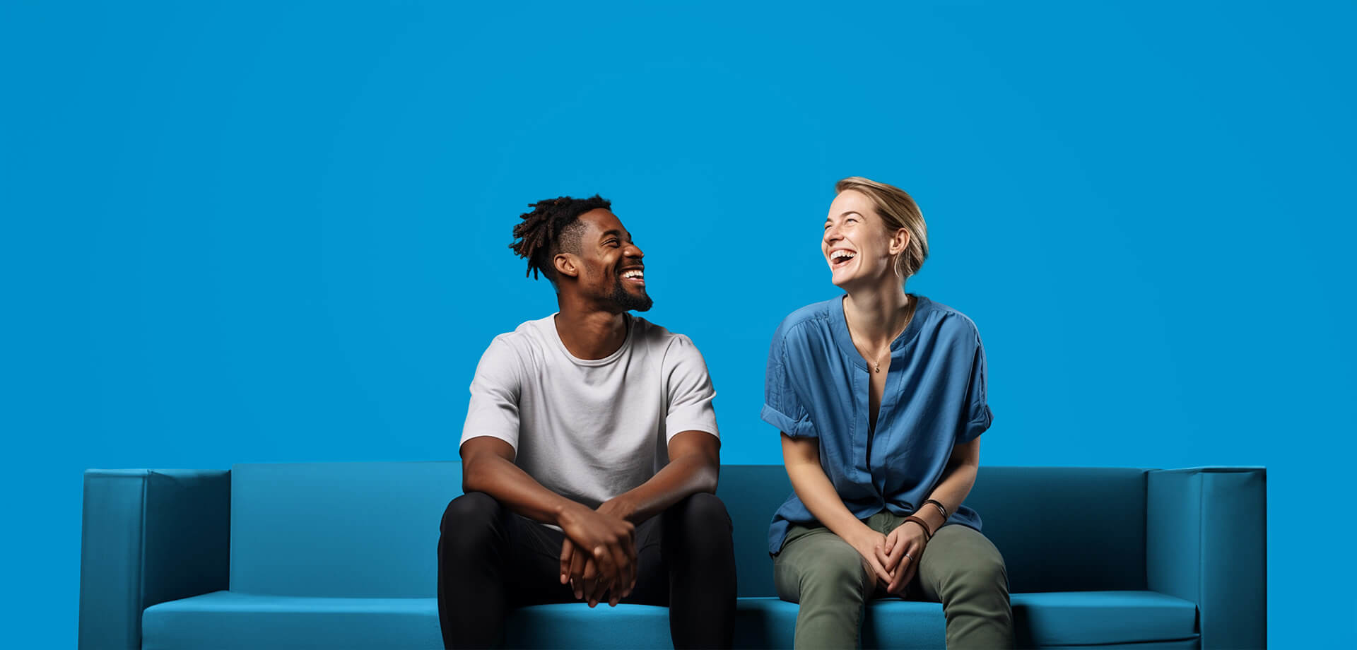 Twee mensen zitten tegenover elkaar op een blauwe bank tegen een heldere blauwe achtergrond en zijn in gesprek.