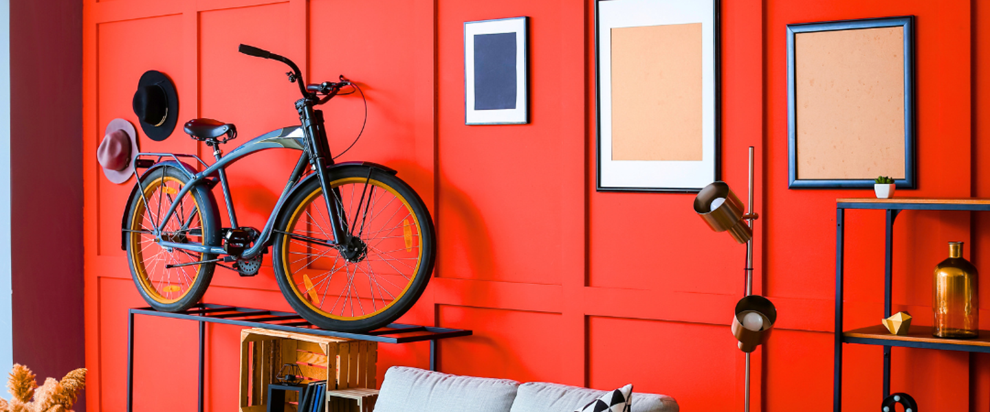 A black bike with yellow tires is parked on a metal rack in front of a vibrant red wall adorned with various artworks.