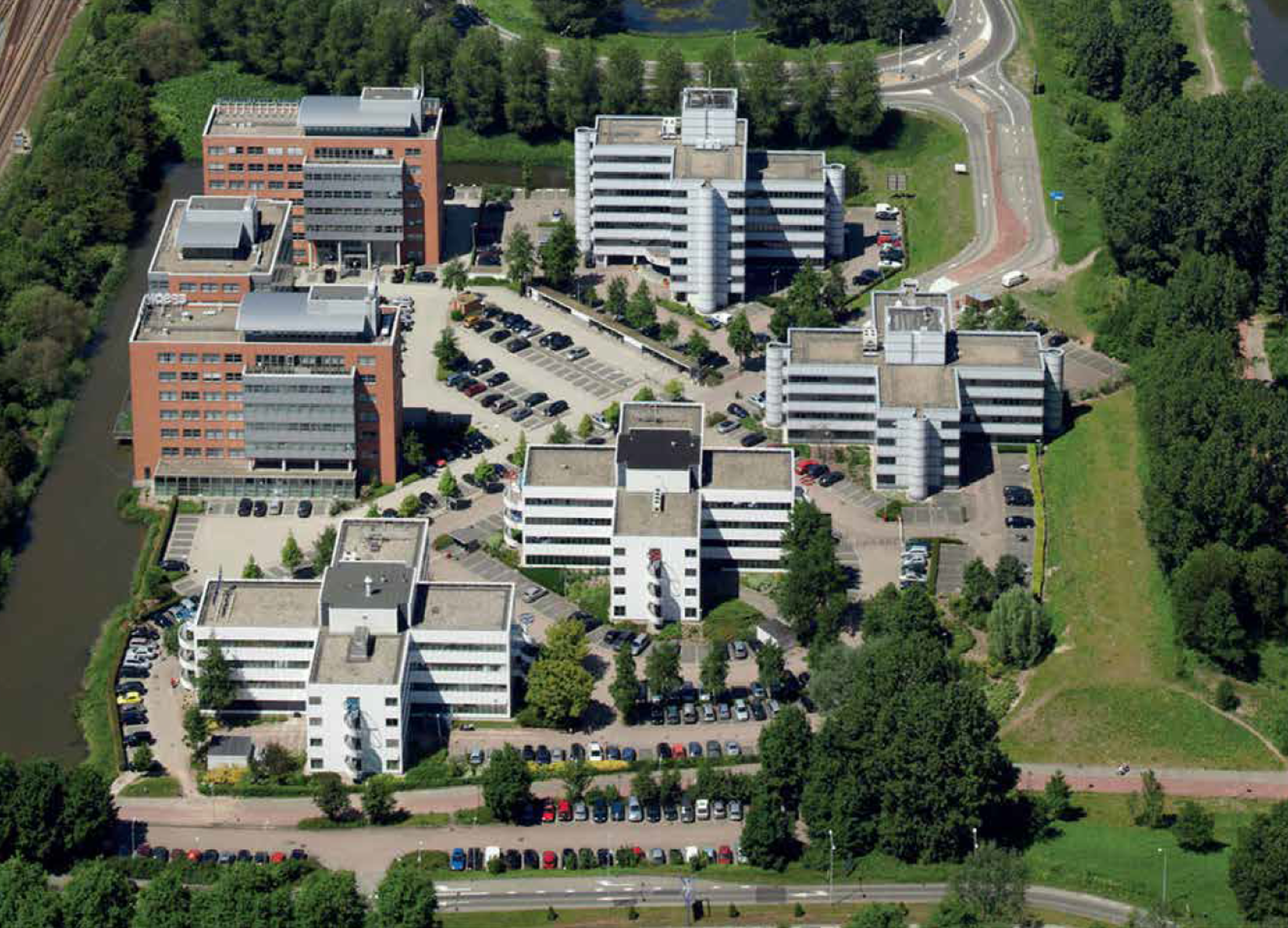 Luchtfoto van een zakendistrict met moderne kantoorgebouwen, parkeerplaatsen en groenvoorzieningen.