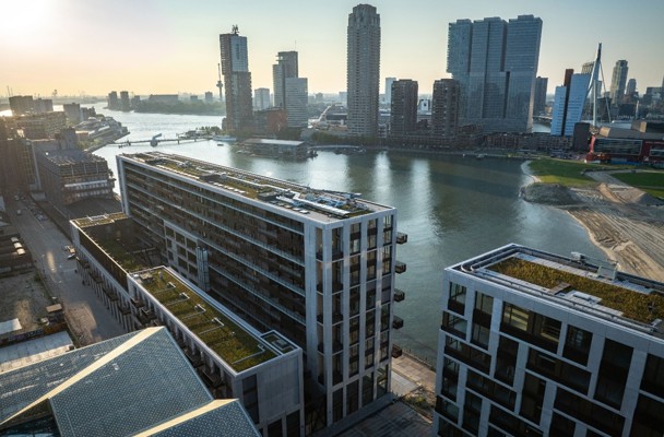 View of modern apartments along a river, with a skyline of tall buildings in the background.