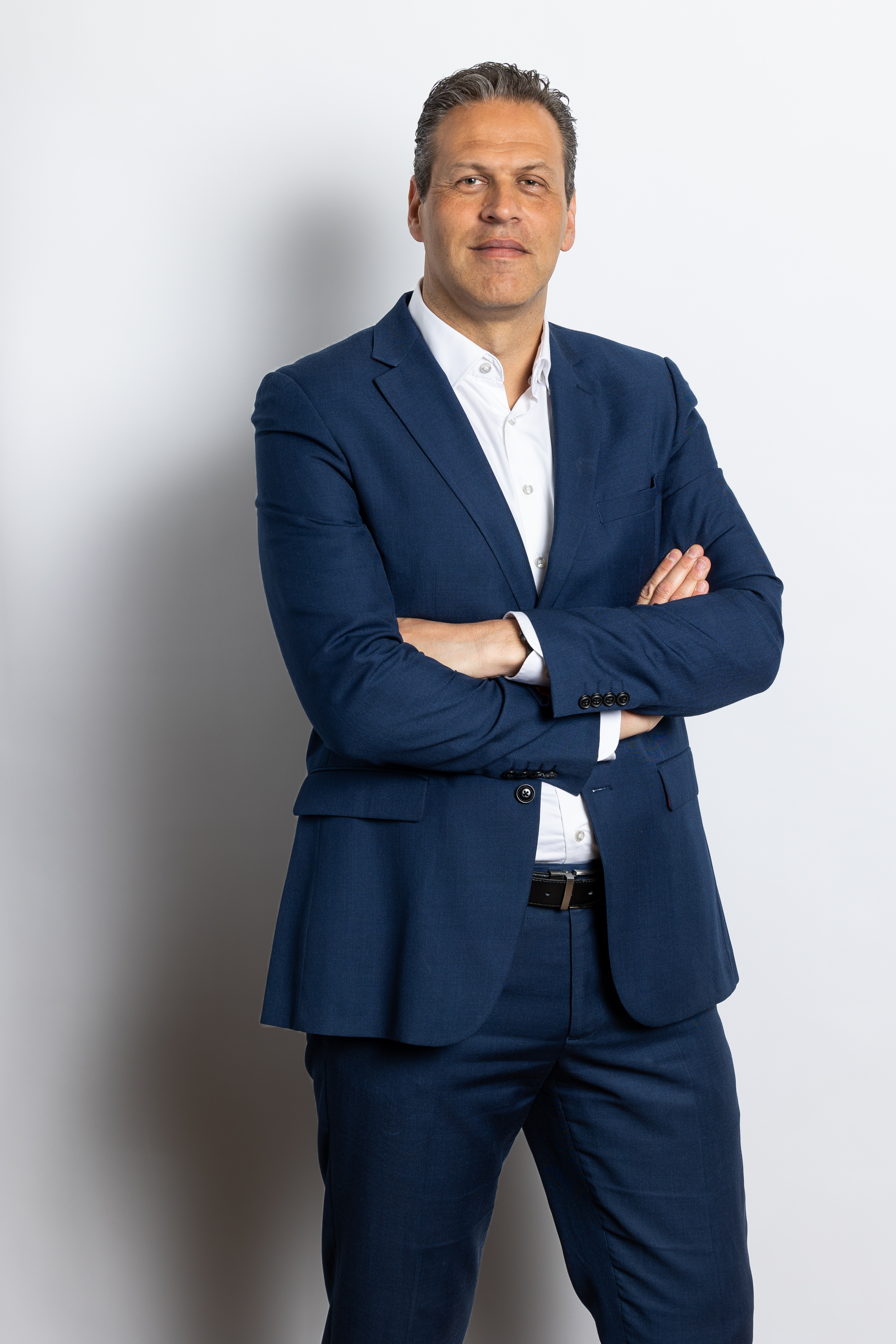 Coen Vreeswijk in een formele donkere blazer met gekruiste armen op een neutrale achtergrond.