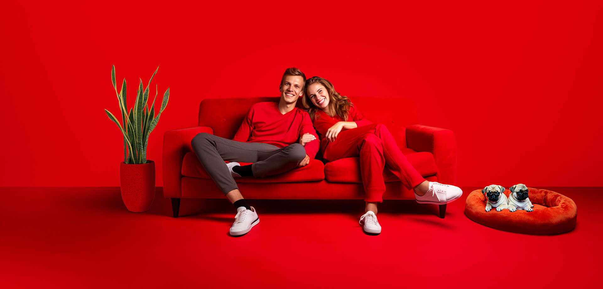 Twee mensen in rode kleding zitten samen op een rode bank, met een groene plant op de achtergrond.