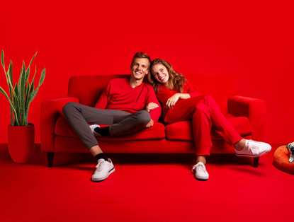 Twee mensen in rode kleding zitten samen op een rode bank, met een groene plant op de achtergrond.