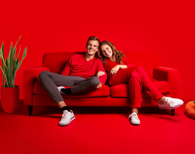 Twee mensen in rode kleding zitten samen op een rode bank, met een groene plant op de achtergrond.