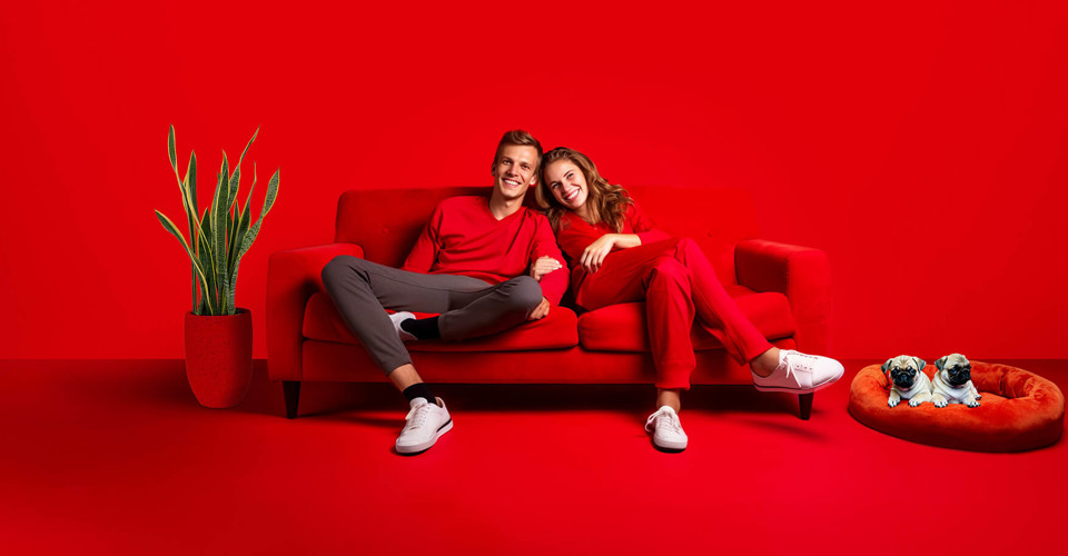 Twee mensen in rode kleding zitten samen op een rode bank, met een groene plant op de achtergrond.