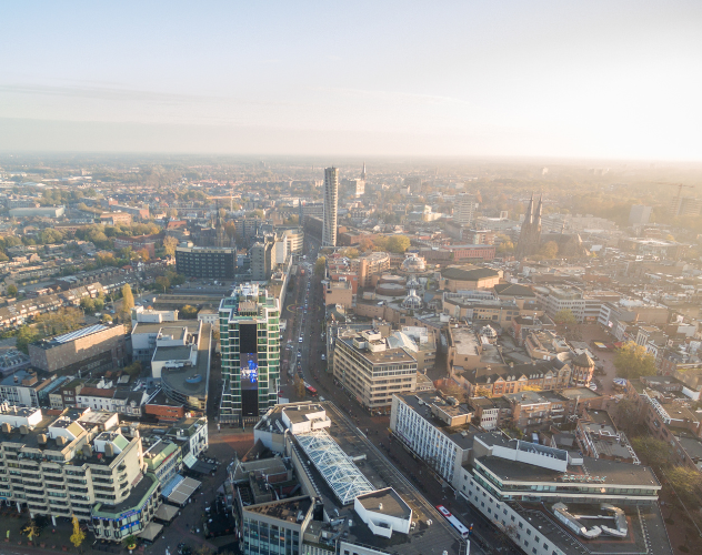 Luchtfoto van een stedelijk gebied met hoge gebouwen, wegen en een heldere lucht.