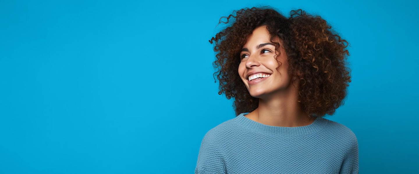 Vrouw met een volle, krullende haardos, gekleed in een lichtblauw shirt, tegen een helderblauwe achtergrond.
