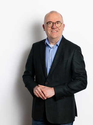 Daan Van Der Ree in een zwart colbert staat rechtop met zijn handen voor zich gevouwen, tegen een witte achtergrond.