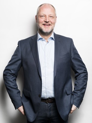 Oscar Langerak in een zakelijke outfit met zijn handen in de zakken, staand voor een lichte achtergrond.