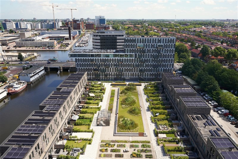 Luchtfoto van moderne appartementencomplexen met groene daken en een gezamenlijke tuin, gelegen aan een haven.