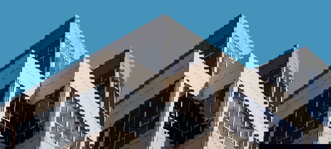 Hoek van een modern kantoorgebouw met grote ramen en een blauwe lucht.