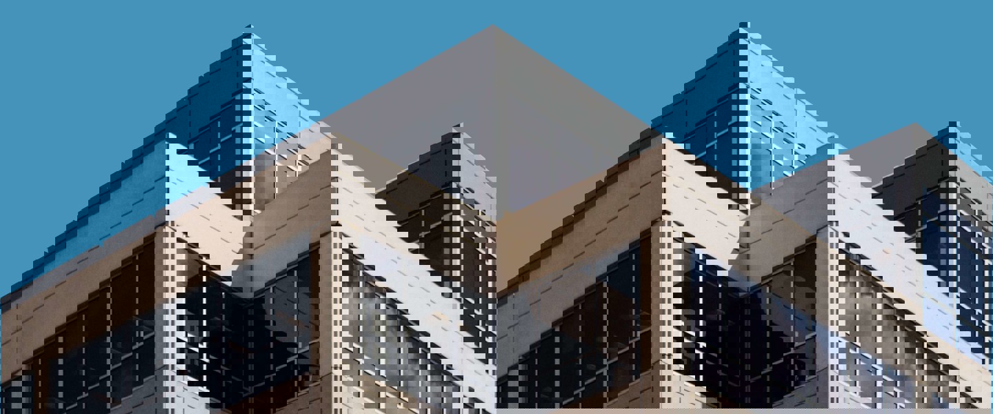 Hoek van een modern kantoorgebouw met grote ramen en een blauwe lucht.