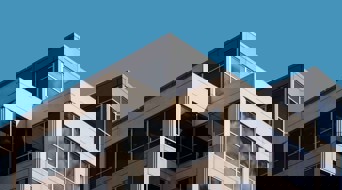 Hoek van een modern kantoorgebouw met grote ramen en een blauwe lucht.