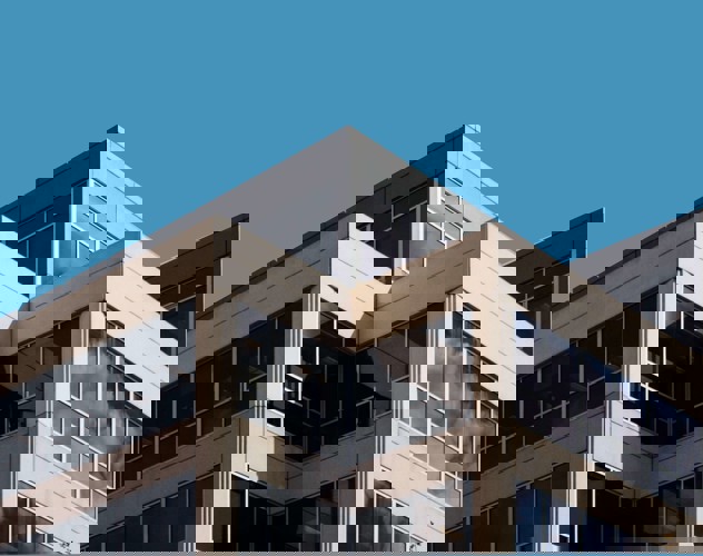 Hoek van een modern kantoorgebouw met grote ramen en een blauwe lucht.