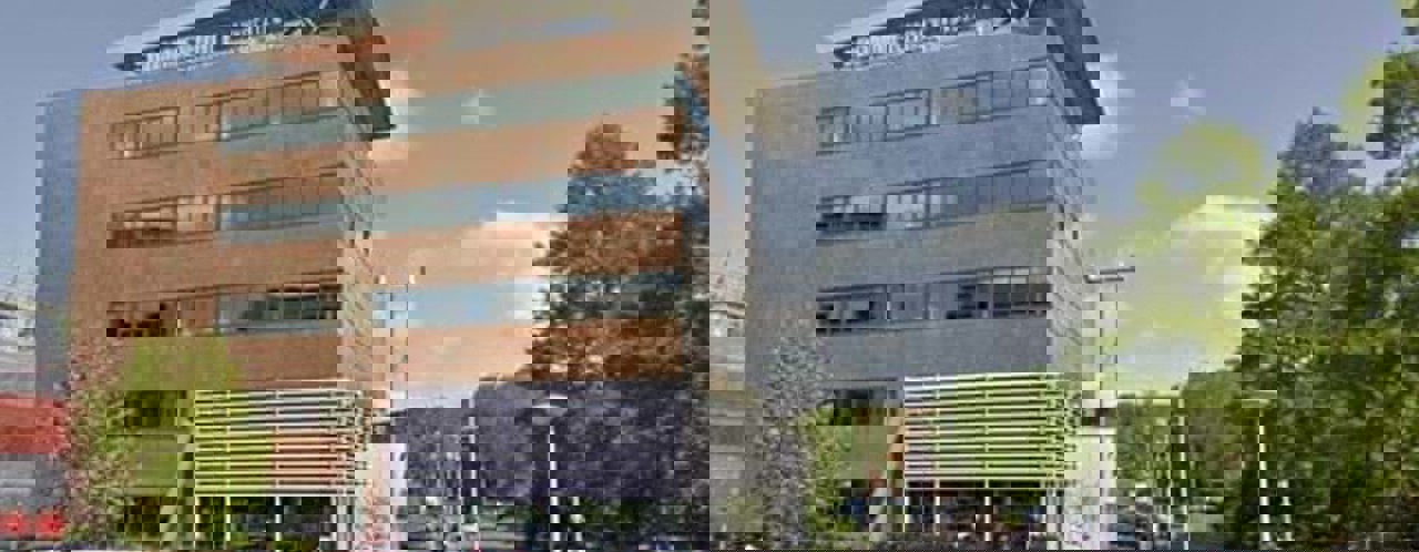 Kantoor van een modern advocatenkantoor, omringd door bomen en parkeerplaatsen.