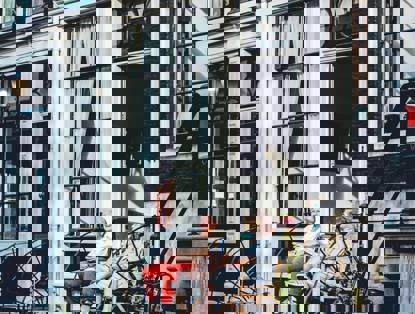 Twee personen zitten op een stoep voor een gebouw met grote ramen, met een schilderij zichtbaar op de achtergrond.