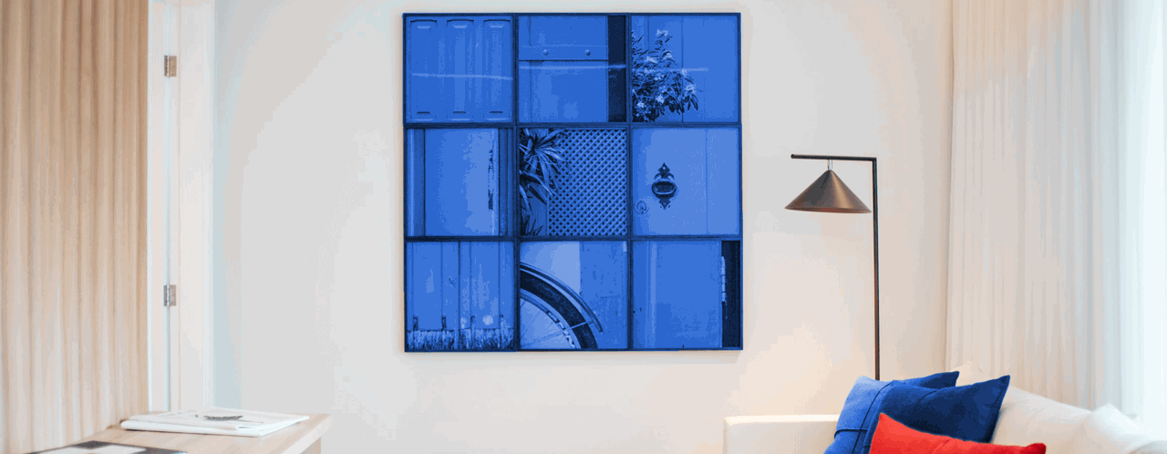 Een moderne woonkamer met een blauw kunstwerk aan de muur, een witte bank met blauwe en rode kussens, en een lamp in de hoek.