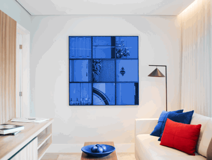 Een moderne woonkamer met een blauw kunstwerk aan de muur, een witte bank met blauwe en rode kussens, en een lamp in de hoek.