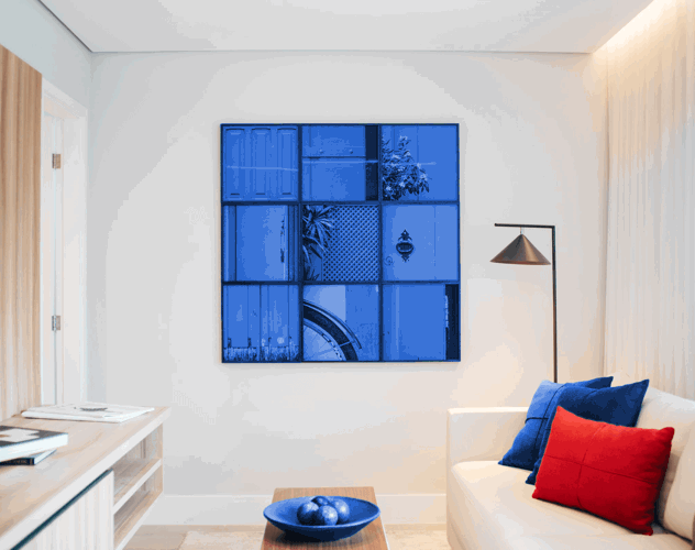 Een moderne woonkamer met een blauw kunstwerk aan de muur, een witte bank met blauwe en rode kussens, en een lamp in de hoek.