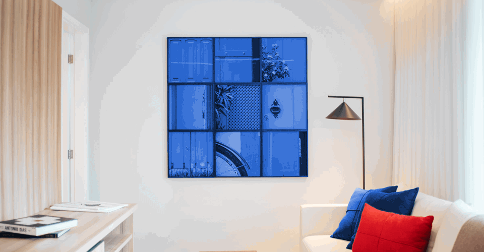 Een moderne woonkamer met een blauw kunstwerk aan de muur, een witte bank met blauwe en rode kussens, en een lamp in de hoek.