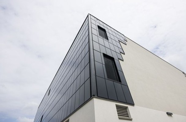 Modern kantoorgebouw met een zwart glanzende gevel en een wit geschilderde muur, onder een bewolkte lucht.