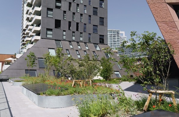 Moderne gebouwen met opvallende, schuine gevels, omgeven door een groene tuin met bloemen en bomen.