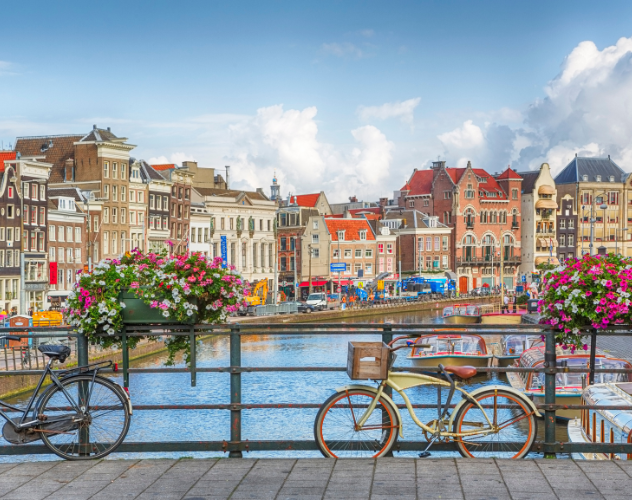 Uitzicht op een kanaal in Amsterdam met op de voorgrond een bloemenversierde brug en twee fietsen tegen de leuning.