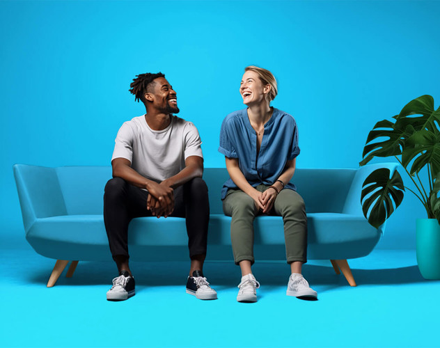 Twee mensen zitten op een lichtblauwe bank voor een felblauwe achtergrond, omringd door een groene plant.